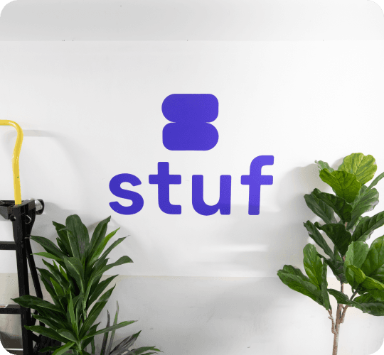 Stuf logo painted on a white wall between potted plants and a hand truck inside a Stuf storage facility
