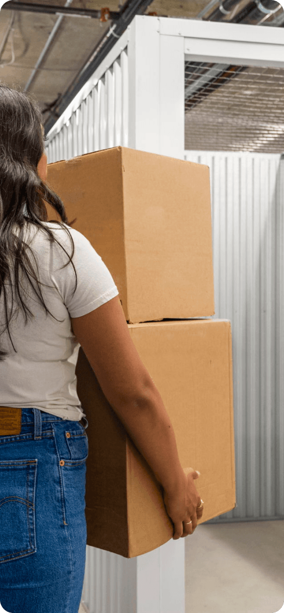 Stuf member carrying two stacked cardboard boxes past a white storage unit inside a facility