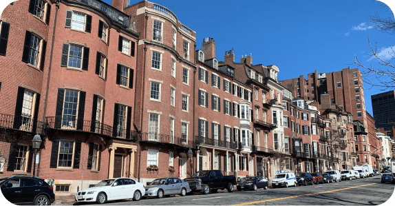 Row of red brick Beacon Hill townhouses lining a Boston street with cars parked along the curb